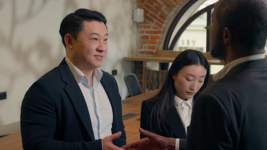 Three business multiracial people multiethnic colleagues diversity coworkers in office meeting two men businessmen African Asian men talk handshaking Japanese Chinese woman businesswoman write notes