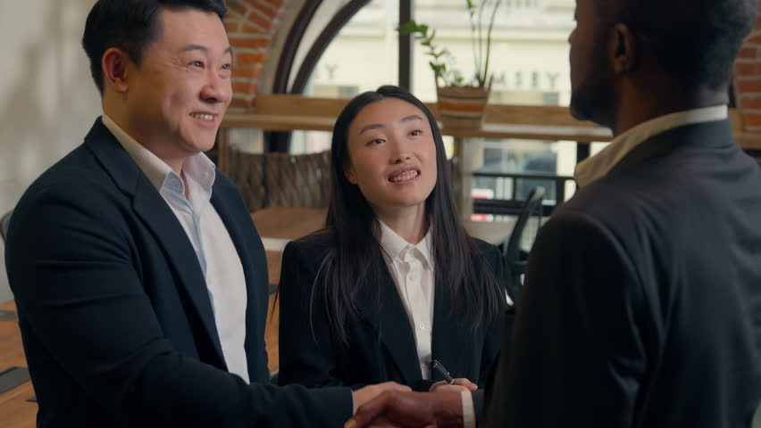 Three business multiracial people multiethnic colleagues diversity coworkers in office meeting two men businessmen African Asian men talk handshaking Japanese Chinese woman businesswoman write notes