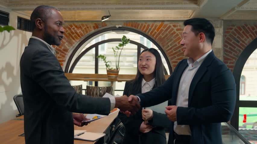 Three multiracial business colleagues coworkers multiethnic in office Asian woman businesswoman Korean Japanese Chinese men businessmen African boss leader talk document discuss pointing data diagram