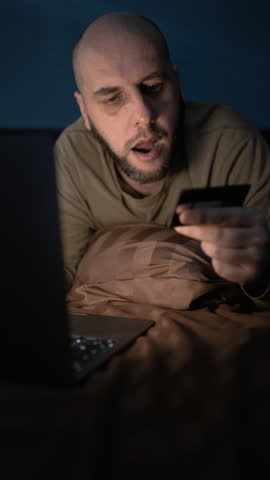 Unhappy bearded man distressed with problems paying online on laptop with credit card. Upset guy at night confused have troubles shopping on computer online.