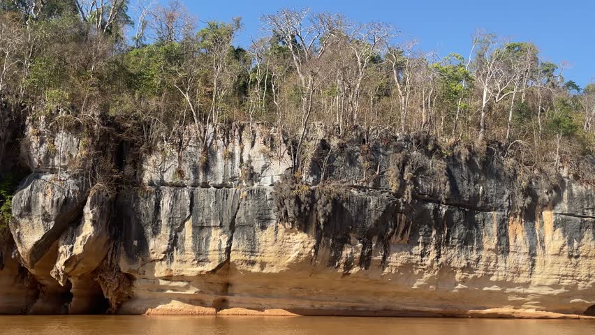 Witness the beauty of the riverbank featuring fascinating rock formations and vibrant foliage under clear blue skies, creating a tranquil atmosphere perfect for nature lovers.