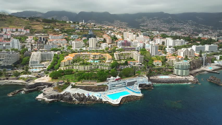 Aerial drone view of Funchal city with hotels resorts and swimming pool along the coast of Atlantic ocean. Funchal, Madeira, Portugal. Orbit parallax shot