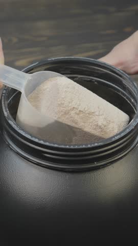 Vertical footage of a man taking mass gainer protein powder for muscle gain in black container. Healthy sports nutrition. Close up spoon for right dose.
