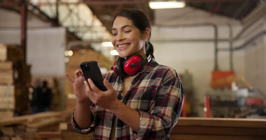 Woodwork, woman and phone with smile in workshop, headphone or safety as noise cancelling for furniture design. Smile, female carpenter and mobile for project, communication and production factory