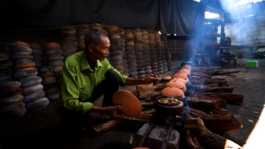 Old man cooking Vietnamese braised pork belly and braised fish in the kitchen, Hoa Hau commune, Ha Nam province, Vietnam near Vu Dai village. Food and travel concept.