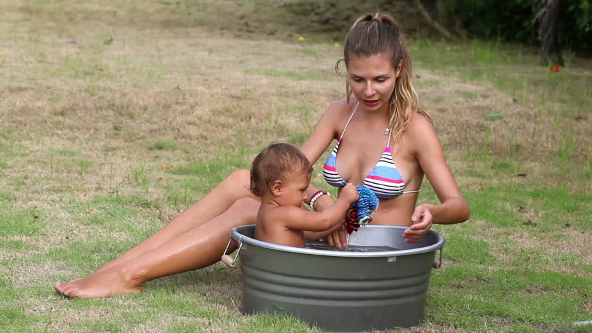 Pretty mother bathes her daughter in washbowl outdoor