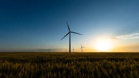 A tranquil scene unfolds as a wind farm stands tall against the backdrop of a setting sun, casting a warm glow over peaceful wheat fields. - Powered by Shutterstock - Get 15% off with code: PIKWIZARD15