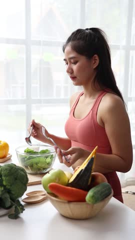 Beautiful healthy Asian woman happily eating delicious vegetable salad at home. Beautiful sport girl in sportswear enjoy eat clean vegetables after exercise for health in house. Diet and Healthy food.