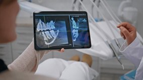 Woman stomatologist holding x-rays on tablet discussing treatment with patient closeup. Unknown dentist explaining digital image at consultation. Professional orthodontist hand scrolling device screen - Powered by Shutterstock - Get 15% off with code: PIKWIZARD15