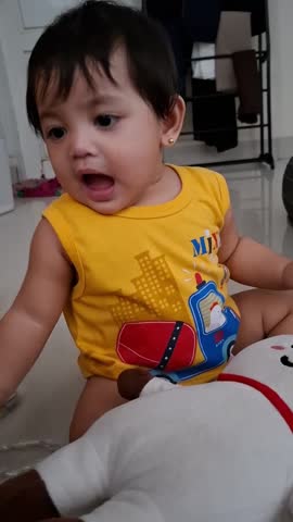 Adorable little girl playing with a white doll while sitting in her bedroom.