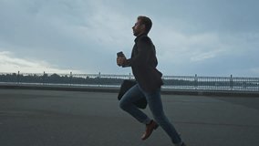 A man in formal attire is seen sprinting along a waterfront promenade as dark clouds gather overhead. The atmosphere suggests urgency amidst a scenic backdrop. - Powered by Shutterstock - Get 15% off with code: PIKWIZARD15