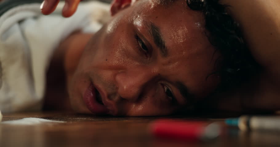 Drugs, addiction and face of man on table with powder, syringe and healthcare danger with narcotics. Mental health, overdose and person with cocaine abuse, fentanyl risk and opioid crisis in home