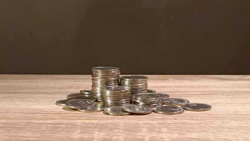Close up of male hand stacking coins on the wooden table. Money saving, cost and budget or investment concept.
