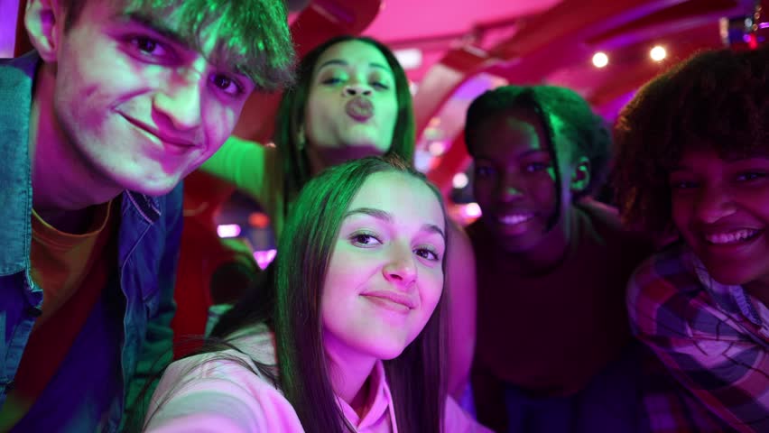Happy group of teenagers taking a selfie together in a vibrant arcade setting, smiling and having fun. Group of Teenagers Smiling and Posing for a Fun Selfie at the Arcade
