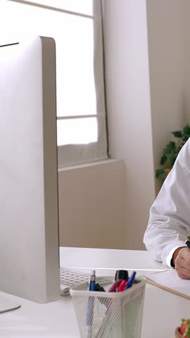 Vertical HD video of young adult female nutritionist doctor consulting patient through desktop video call, taking notes while listening.