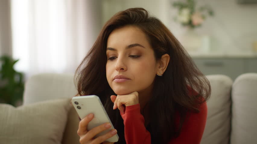 Bored thoughtful Caucasian female tired woman girl client user boredom typing message chatting using mobile phone scrolling social media boring online app thinking problem solution at home living room
