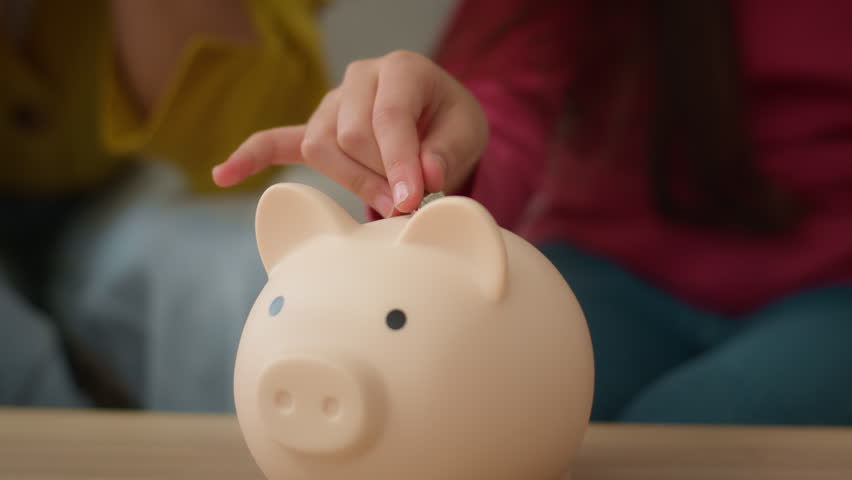 Unknown family female woman and little girl child kid hands putting coins in piggy bank hoarding coin saving money save finance cash investment accumulation business financial security indoors home