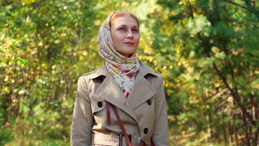 A young woman stands in an autumn forest, breathing in fresh air and admiring nature. An autumn sunny day for human inspiration.
