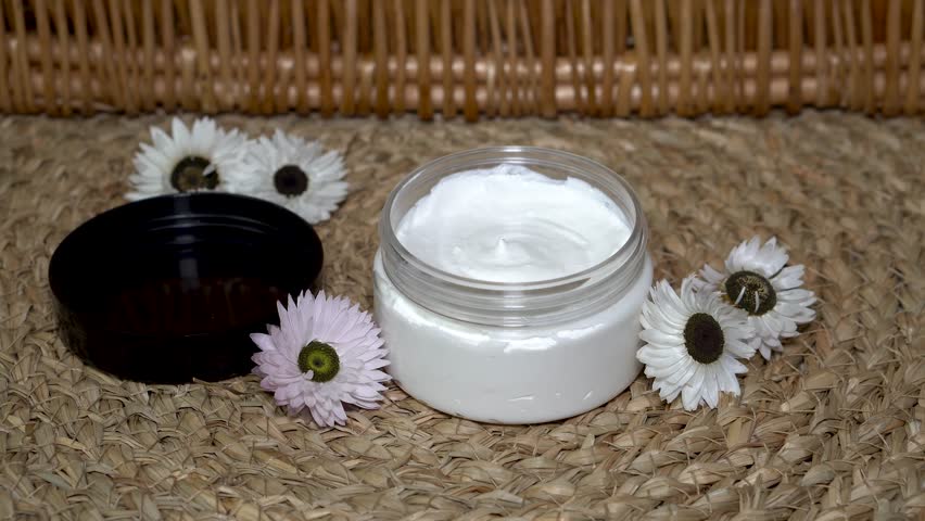 A woman showing homemade cream in transparent packaging. Natural sunscreen on beige background with flowers.