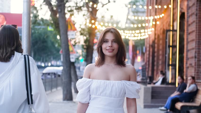 Portrait of a beautiful young woman in a cute white dress on a city street in the evening