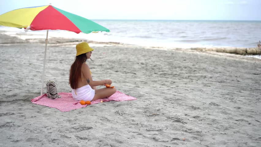 Woman eating mandarins under a colorful beach umbrella