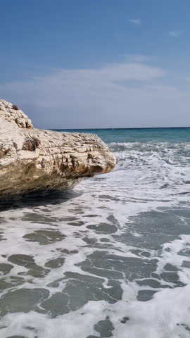 Turquoise sea waves crashing against white rock on sunny day. Vertical video.