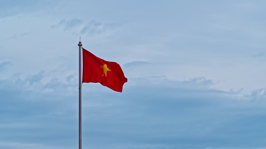 Vietnamese flag on the flagpole flutters in the wind against a cloudy sky