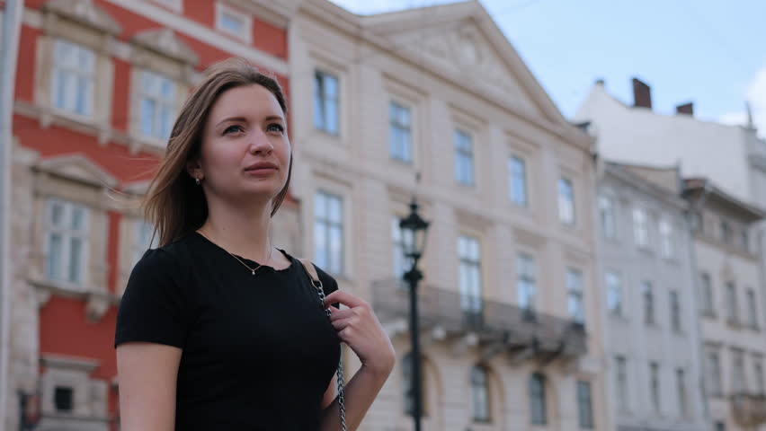 Woman chatting, urban scene, woman talking. Joyful woman stands in urban environment, holding phone to her ear with historic buildings behind her.