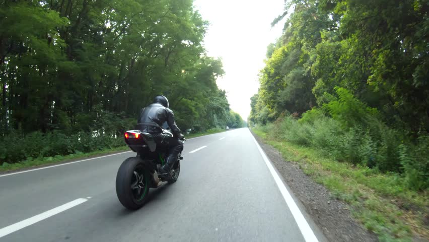 Motorcyclist races motorcycle on woodland country road. Man in helmet rides on sport motorbike at rural road near forest. Guy driving bike during trip. Concept of freedom and adventure. Aerial shot