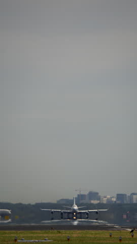 Vertical video of a large passenger airplane taking off from the runway with distant buildings in the background