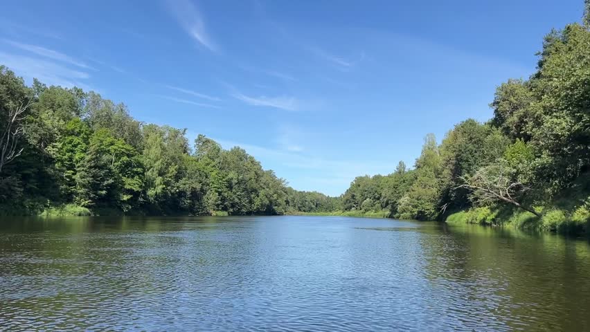 A calm river with trees on both sides. The sky is clear and blue. The water is still and peaceful