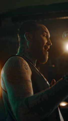 Vertical close-up of bearded young Caucasian male vocalist standing on stage with microphone smiling, enjoying groove and pleased with fame
