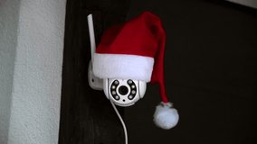 White CCTV camera in red Santa Claus hat rotates and records moving objects. Outdoor video surveillance. Security system. Web cam. Web street control. Distance watch. Smart tech. Footage. Copy space. - Powered by Shutterstock - Get 15% off with code: PIKWIZARD15