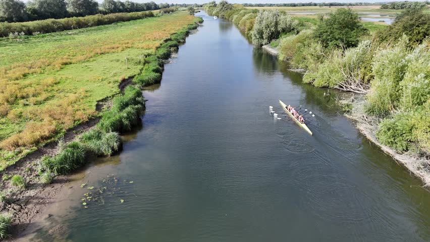 Drone shot following rowing sculling quad boat yellow along river in sunshine with nature on banks