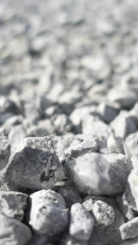 Background of gray granite gravel under the bright sun. Stock footage. Close up of white stones falling down on the ground, pebble texture.
