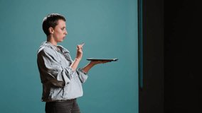 Modern tech person operating on tablet with a futuristic hologram, innovative visual graphics against blue background. Young woman looks at a holographic 3d image visualization. Camera A. - Powered by Shutterstock - Get 15% off with code: PIKWIZARD15