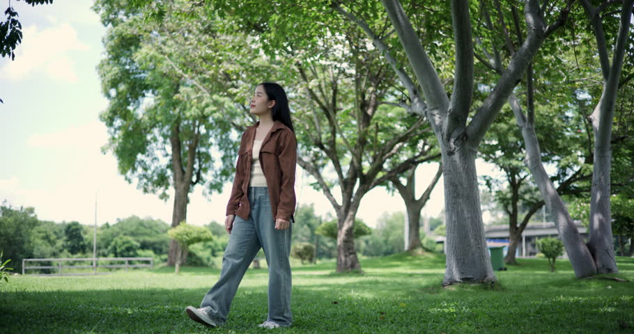 Footage handheld shot, Happy young woman enjoys a relaxing walk in a park, Enjoying the fresh air and the beauty of nature around her.