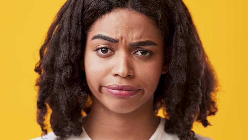A young woman with curly hair displays an exaggerated facial expression, rolling her eyes while looking slightly annoyed. The bright yellow backdrop enhances the dramatic effect of her expression.