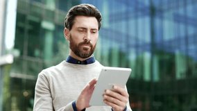 Confident serious businessman using a digital tablet outside modern urban office building, focused and engaged with technology on city street. Thoughtful man texting, chatting online, browsing the web - Powered by Shutterstock - Get 15% off with code: PIKWIZARD15