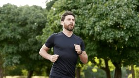 Handsome male runner jogging in an urban city park and looking smart watch. Bearded athlete using fitness tracker. Sportsman checking result. Adult fit man in T-shirt enjoys running outdoors in nature - Powered by Shutterstock - Get 15% off with code: PIKWIZARD15