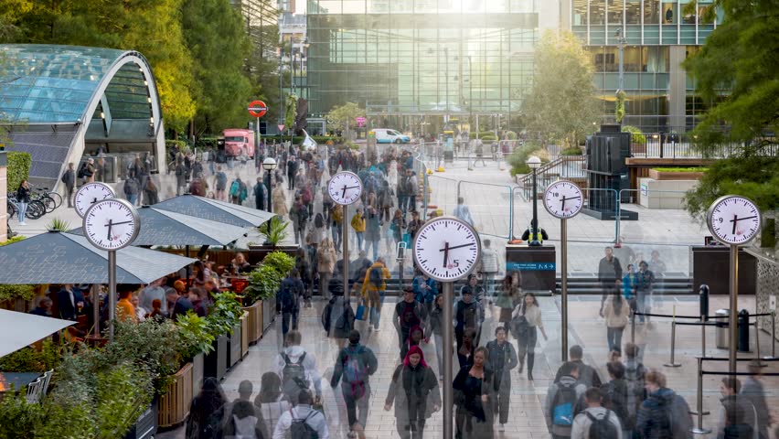 Timelapse view of motion blurred business people rushing from work with analogue clocks in front at the financial centre Canary Wharf