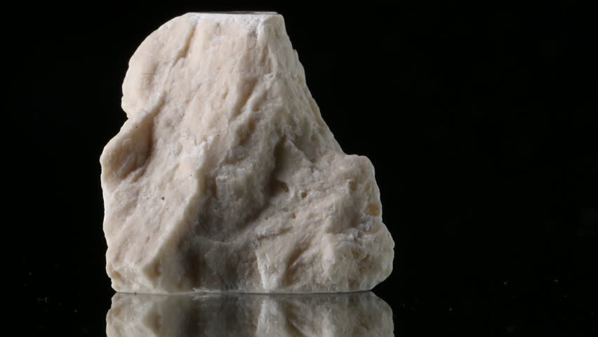 White aragonite (calcium carbonate) sample rotating against a black background
