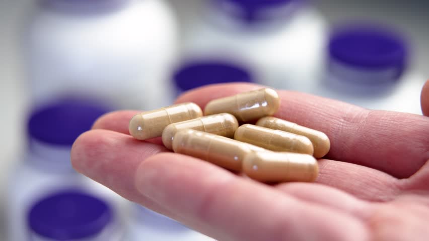 Hand holds natural capsules filled with herbal ingredients and extracts, surrounded by pharmaceutical containers. Alternative medicine supplements concept