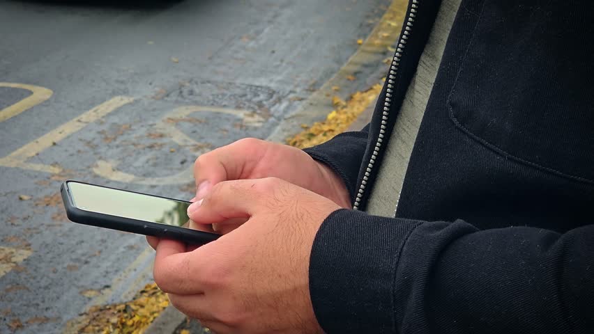 Close up man quickly scrolling through news feed on social networks phone at bus stop. Cinematic close up shot of finger of man touching screen of modern smartphone