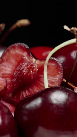 Vertical video. Hand Squeezing Juice from Cherry Half, Berries on Black Background, Macro. Slow Motion.