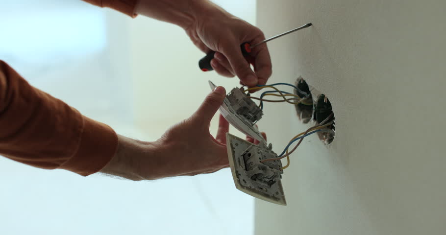 Professional electrician working on a home electrical system. Close up man installing a wall socket at new apartment or house.