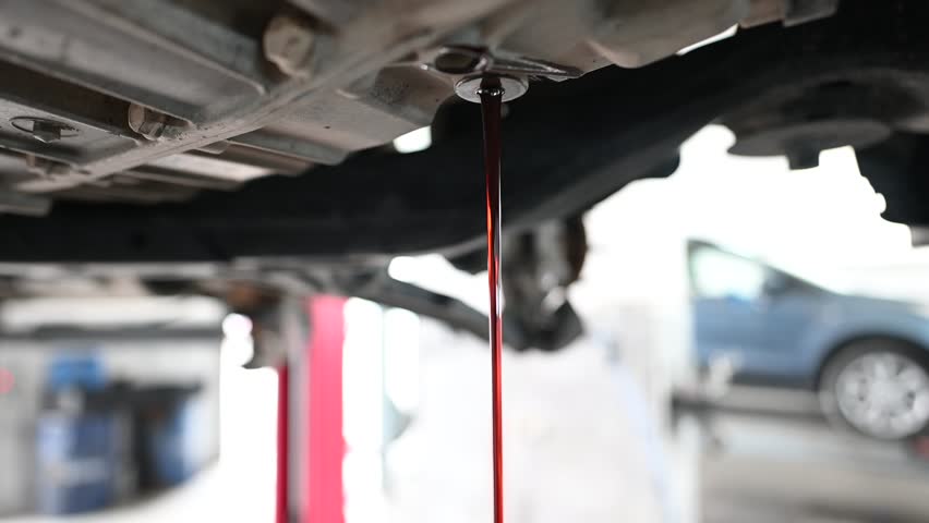 Used engine oil drains from a car engine into a pan. Car maintenance and repair, oil change service concept. Close up.