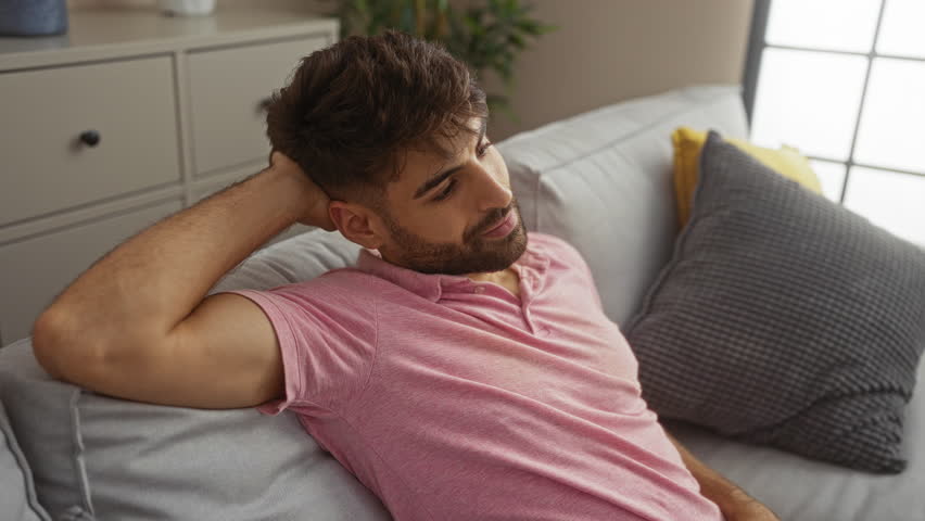 Young man smiling while relaxing on a cozy sofa in a bright apartment living room