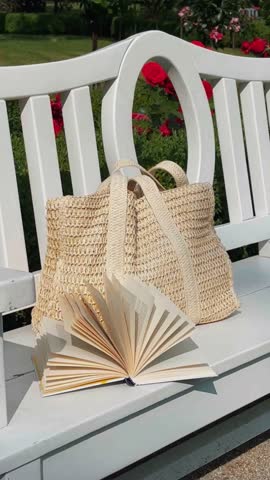 Sunny day. Rest in nature. The book lies on a bench in the rose garden. flower garden White bench. White woven bag