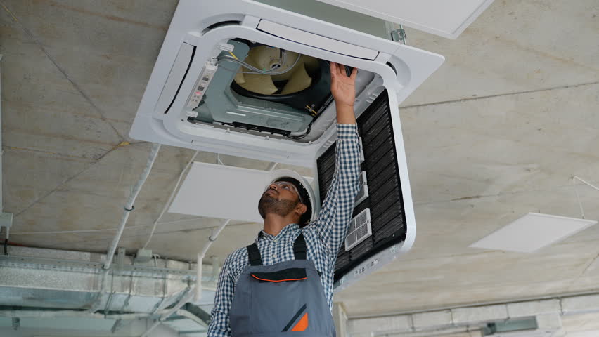Indian HVAC technician performing air conditioner installation in a modern office